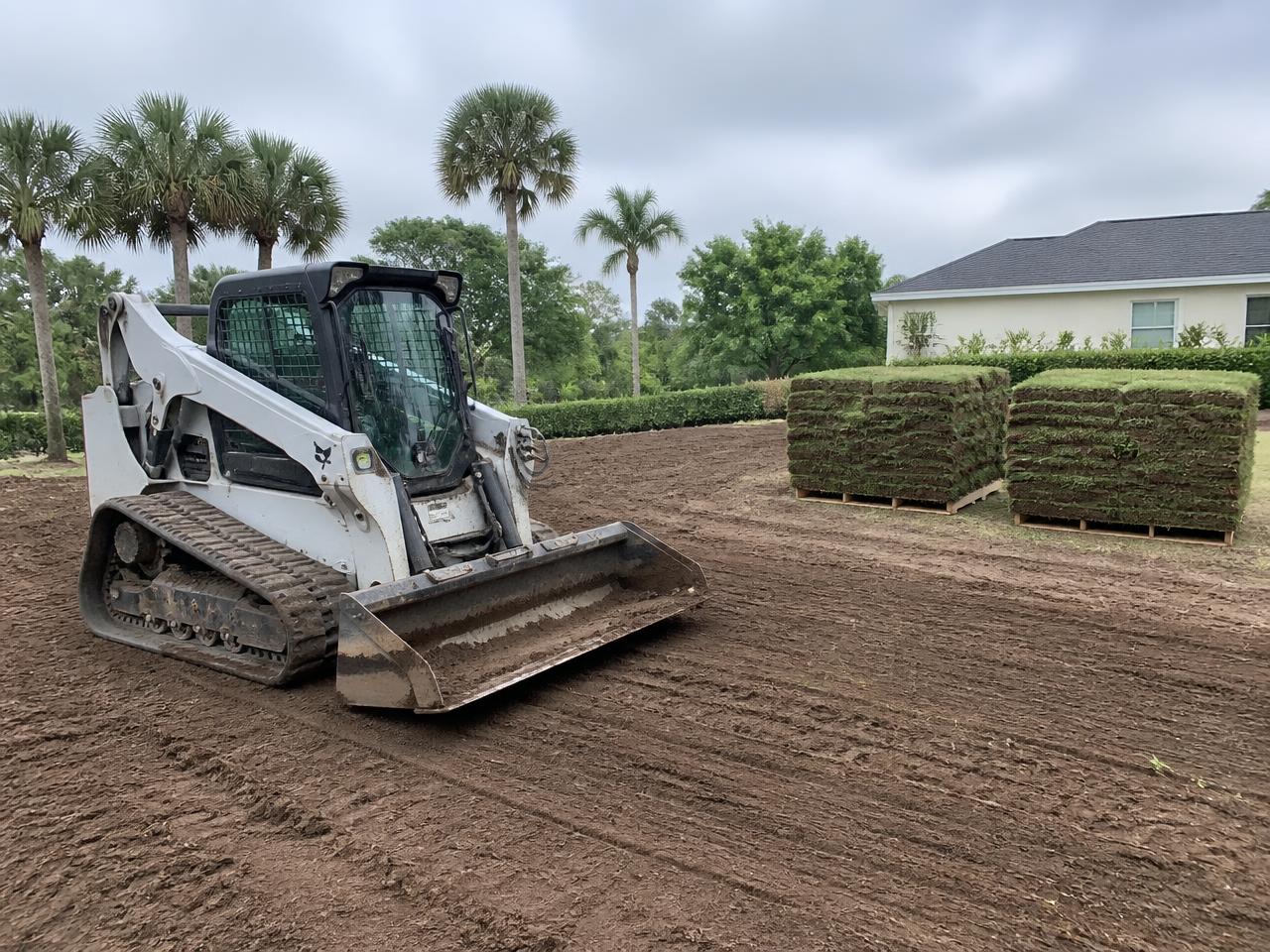 Compact loader grading a Florida yard with pallets of fresh sod waiting to be laid